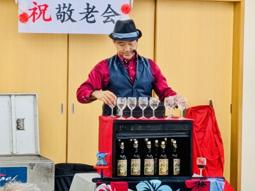 マジシャンJUNPEIが三重県鳥羽市の敬老会イベントでマジックショーを披露している様子。とっても盛り上がっている中グランドフィナーレでグラスタワーを準備している。